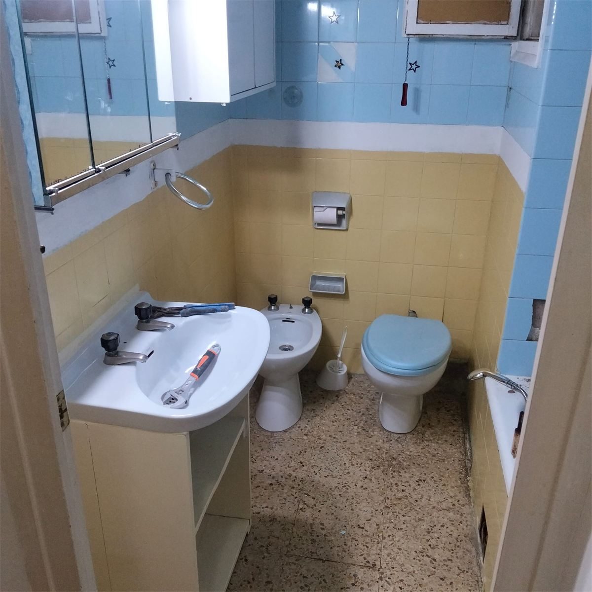 Baño antes de la reforma, con azulejos azules y amarillos y sanitarios antiguos